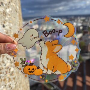 Sticker attrape-soleil holographique représentant un corgi orange et blanc touchant le nez d'un petit fantôme, avec citrouilles, étoiles et lune