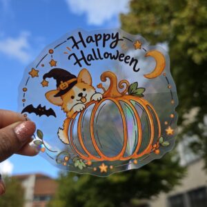 Sticker attrape-soleil holographique Halloween avec un corgi en chapeau de sorcière derrière une citrouille, photographié à la lumière du jour